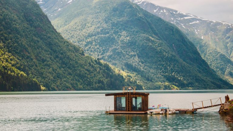 kobieta medytująca na zielonym klifie z panoramicznym widokiem na norweskie fiordy i morze