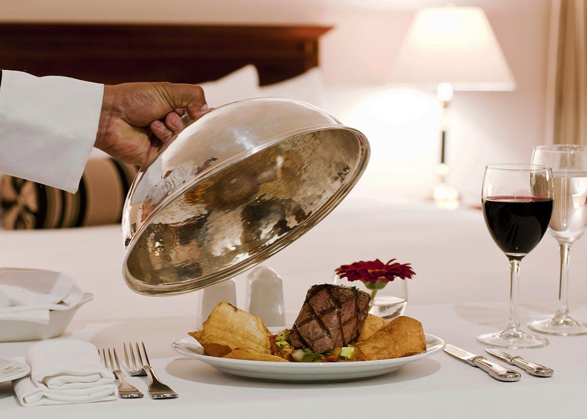 Kelner w uniformie pcha wózek z talerzami jedzenia i napojami przed drzwiami luksusowego hotelowego pokoju