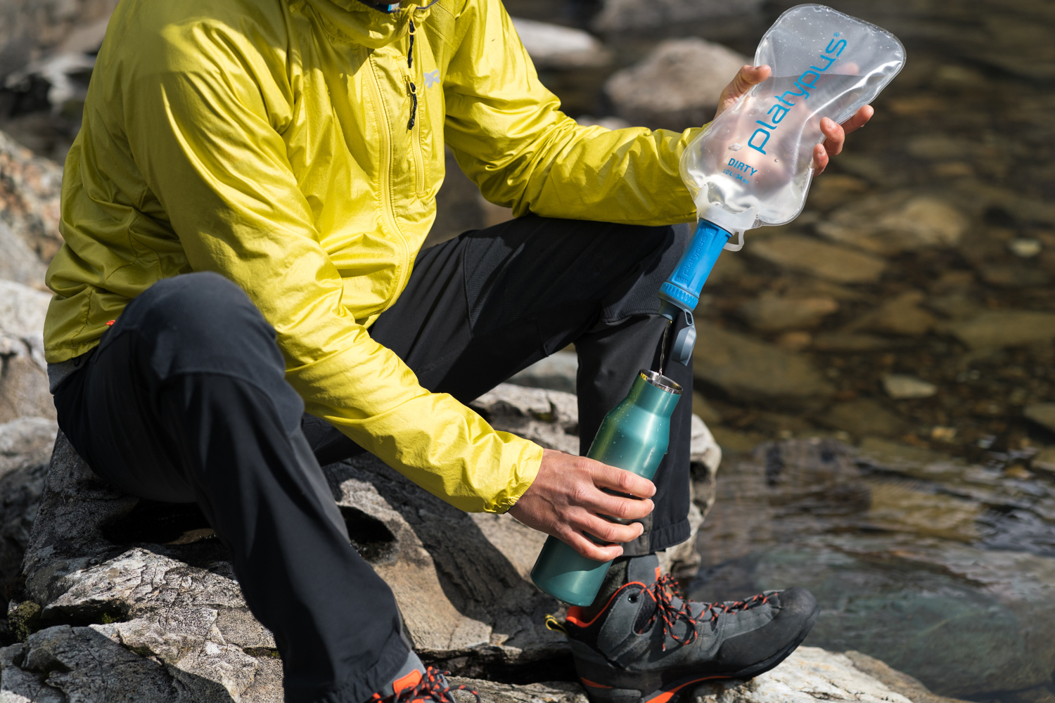 mężczyzna zanurzający filtr w brudnym strumieniu leśnym podczas marszu